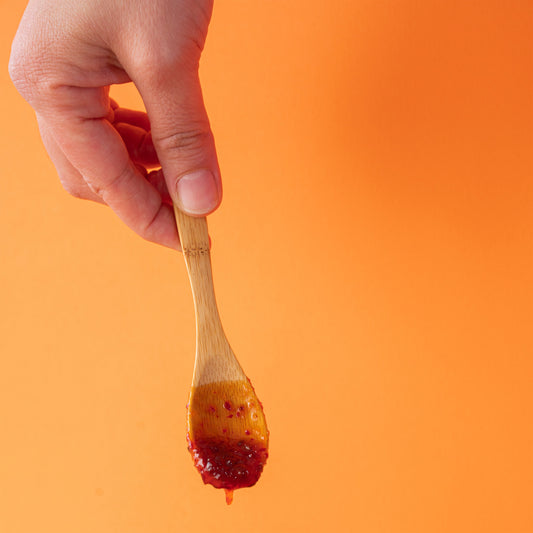 Mão a segurar uma colher de madeira com doce de malagueta malcriado a escorrer.