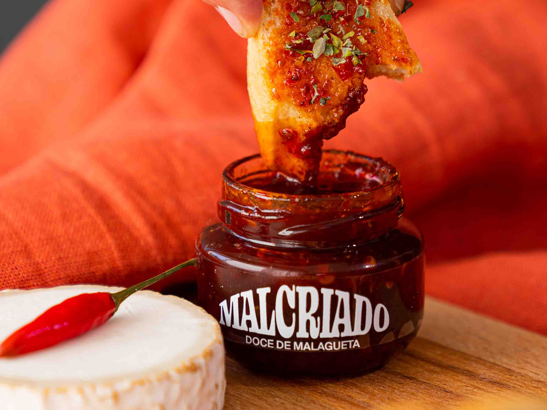 Frasco de doce de malagueta malcriado junto de um queijo de cabra